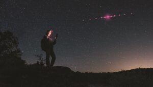 Photoillustration: Hiker using mobile device while magenta-tinted satellites orbit in the sky above