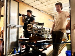James Penna and Finn van Donkelaar stand beside a complicated-looking Jet Gun prototype in the back of a panel truck