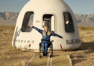 Michaela Benthaus spreads her arms as she sits in a wheelchair outside the Blue Origin crew capsule