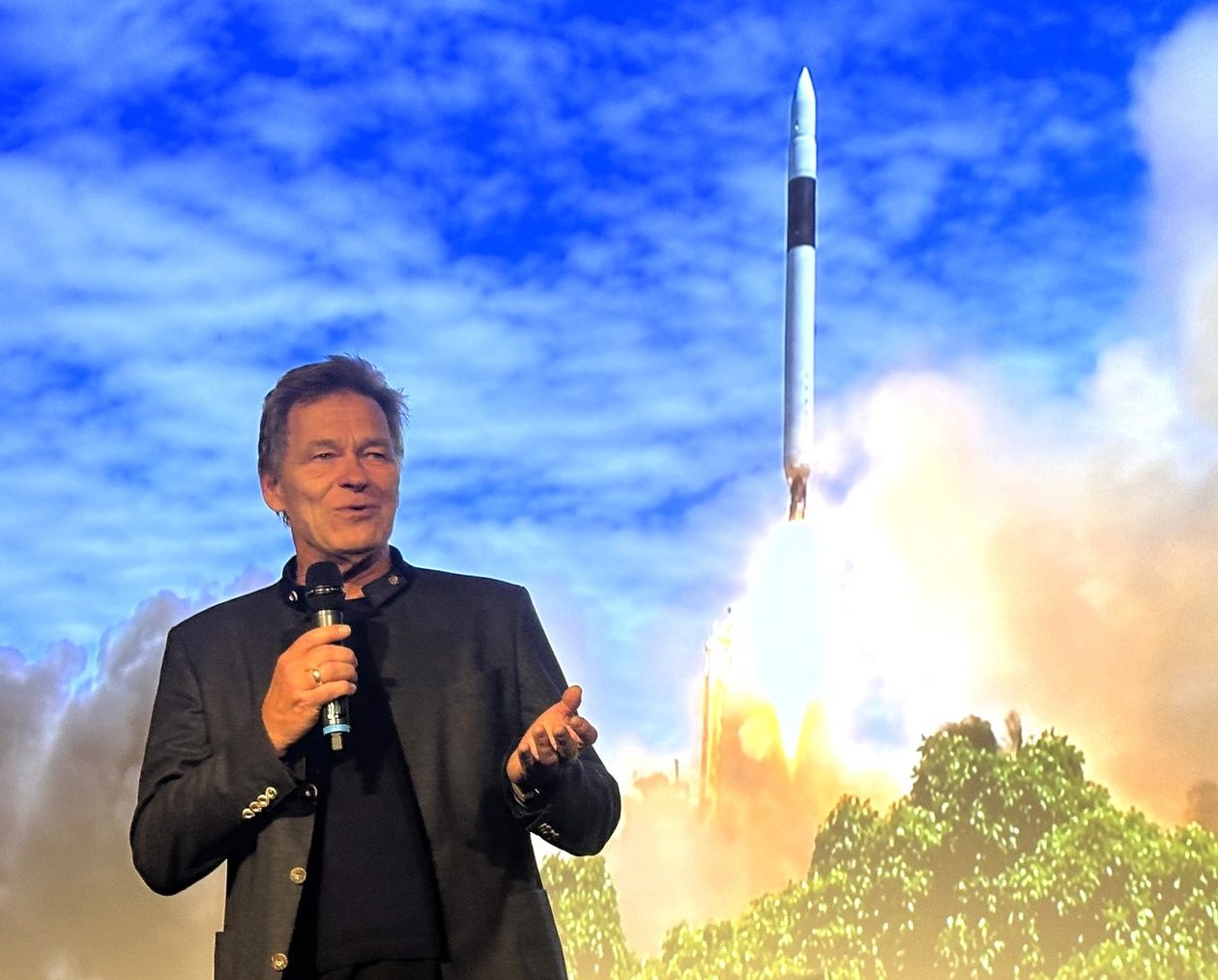 Hans Koenigsmann in front of picture of Falcon 1 launch