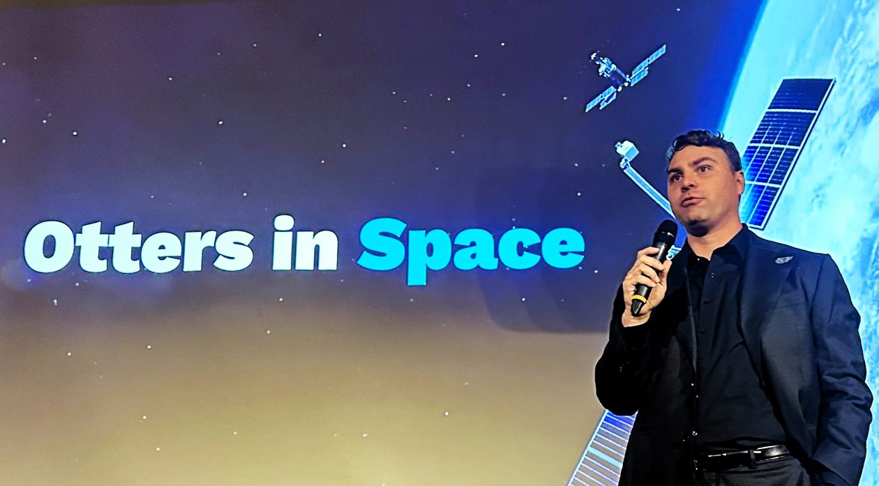 Trevor Bennett speaking in front of screen showing the words "Otters in Space"