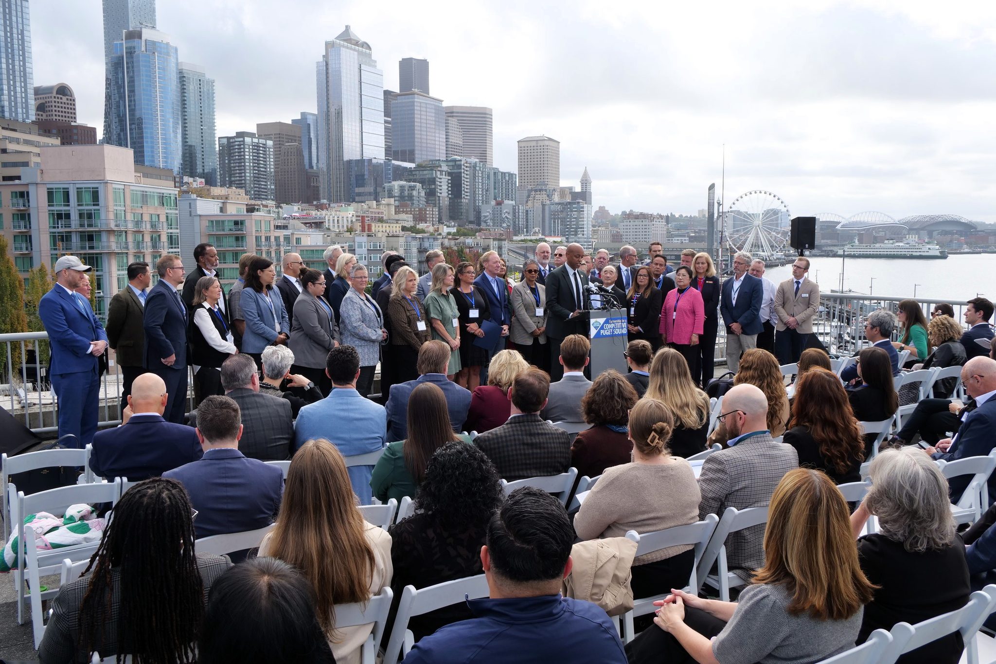 King County Executive Girmay Zahilay addresses attendees Monday against the backdrop of downtown Seattle. According to a new regional report, more than 32% of office space in the city’s central business district is vacant. (GeekWire photo / Todd Bishop)