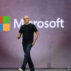 Satya Nadella walks across a stage in front of a large Microsoft logo.