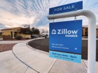 A blue Zillow Homes for-sale sign in front of a house on a residential street.
