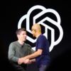 Sam Altman and Satya Nadella shake hands on stage in front of the OpenAI logo