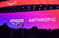 Two men stand on a stage in front of large screens showing the Amazon and Anthropic logos, with an audience in the foreground.