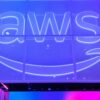 Illuminated AWS logo with the Amazon smile arrow on a glass wall in blue and purple light.