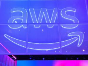 Illuminated AWS logo with the Amazon smile arrow on a glass wall in blue and purple light.