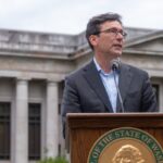 Washington Gov. Bob Ferguson speaks at a podium bearing the state seal in front of a columned building in Olympia.