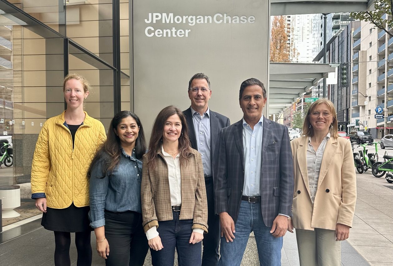 Six JPMorganChase Seattle Tech Center leaders stand on a downtown Seattle sidewalk in front of a pillar with a sign that reads "JPMorganChase Center."