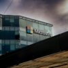 Microsoft logo on a glass office building under a cloudy sky