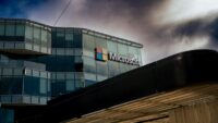 Microsoft logo on a glass office building under a cloudy sky
