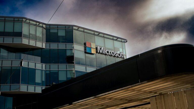 Microsoft logo on a glass office building under a cloudy sky