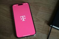 A smartphone showing the T-Mobile logo on a pink screen, lying on a wooden table.